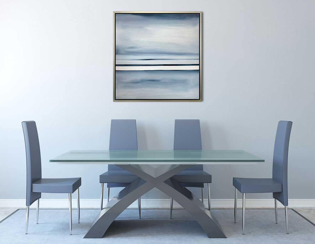 Blue and white abstract painting hangs in a silver floater frame above a glass table with four blue high back chairs.