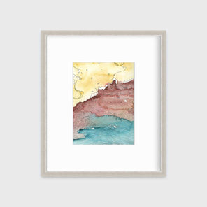 A yellow, dark red, teal and black abstract landscape print in a silver frame with a mat hangs on a white wall.
