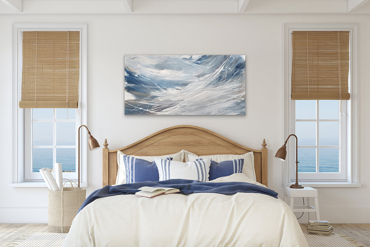 A white, blue, and grey abstract painting by Teodora Guererra hangs on a white wall between two windows and above a queen size bed. The bed has beige bedding with blue and white striped decor pillows. Two white night stands sit on either side of the bed with brown lamps.
