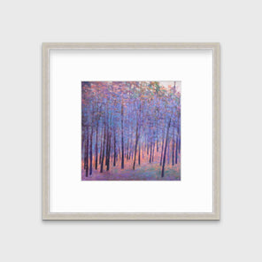 A blue and pink abstract tree landscape print in a silver frame with a mat hangs on a white wall.