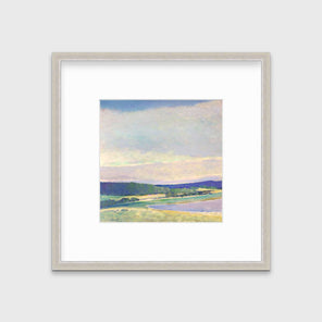 A blue, green and purple abstract landscape print in a silver frame with a mat hangs on a white wall.