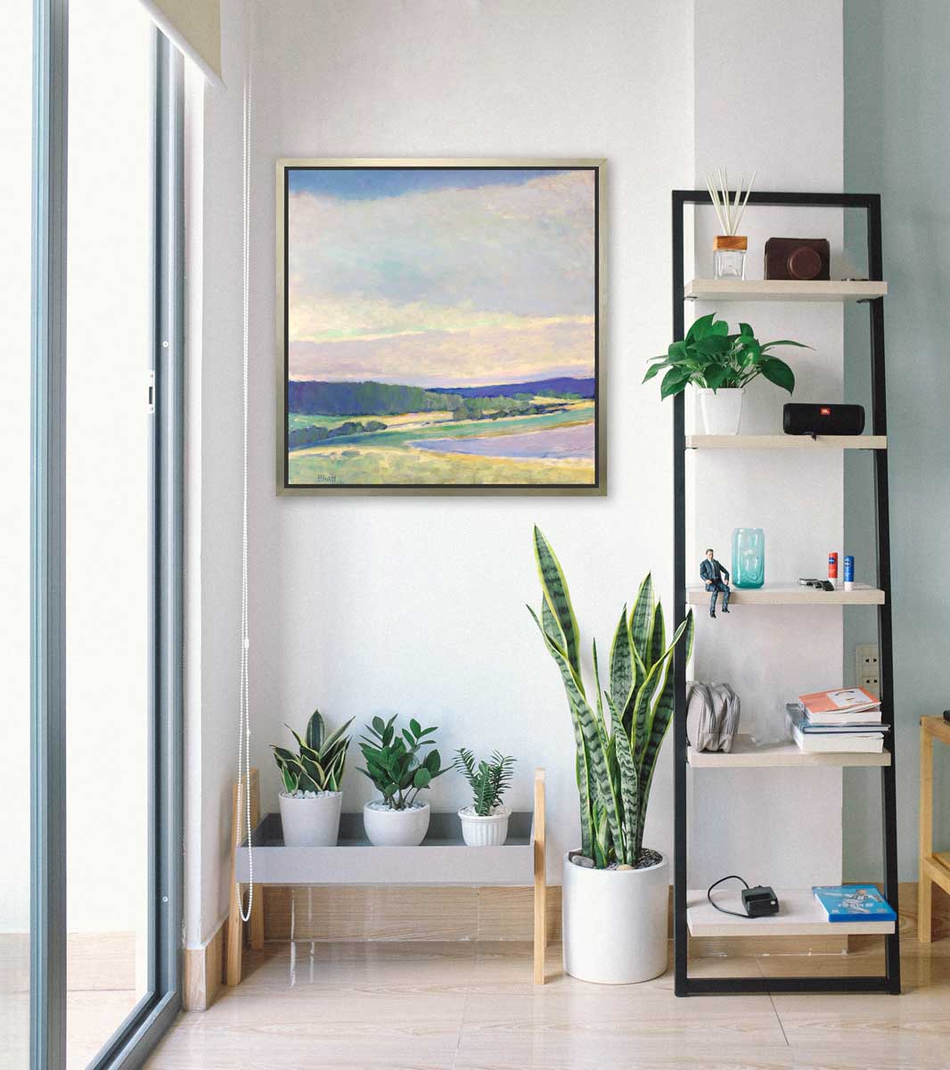 A multicolored abstract landscape print in a silver floater frame hangs on a white wall above a low bench with three potted plants, a medium potted plant and a ladder shelf with accessories.