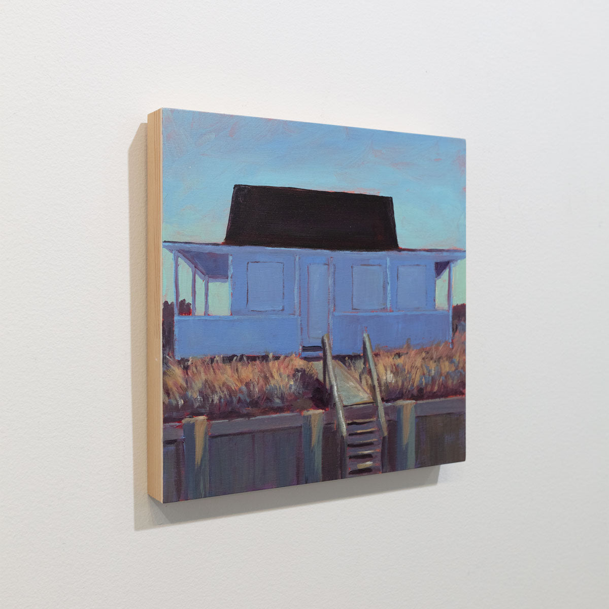A small painting of a blue house with steps is seen at an angle on a gallery wall.