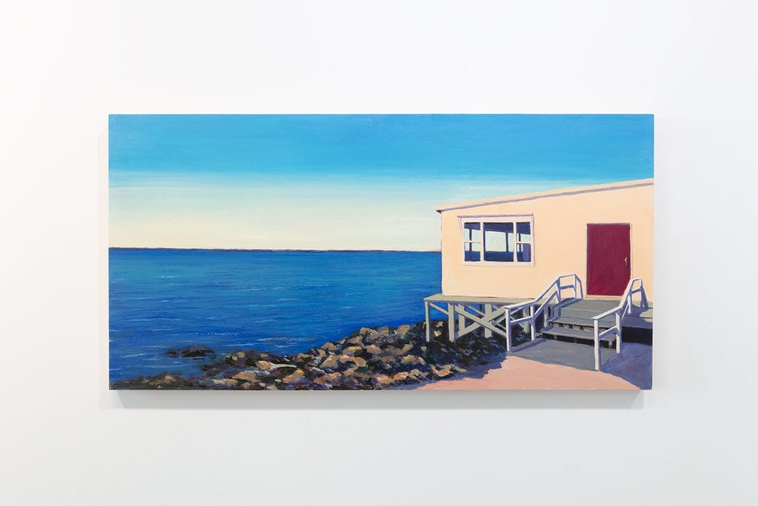 A painting of a house on the water is hung on a gallery wall.