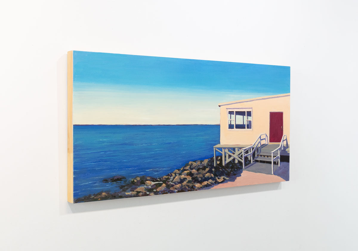 A painting of a house on the water is seen at an angle on a gallery wall.
