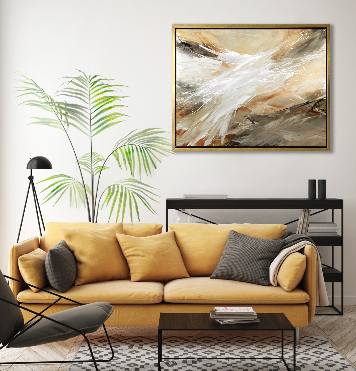 A beige, grey, white and black abstract print in a gold floater frame hangs on a white wall above a dark yellow sofa with pillows, a black three shelf bookshelf and a large potted floor plant.