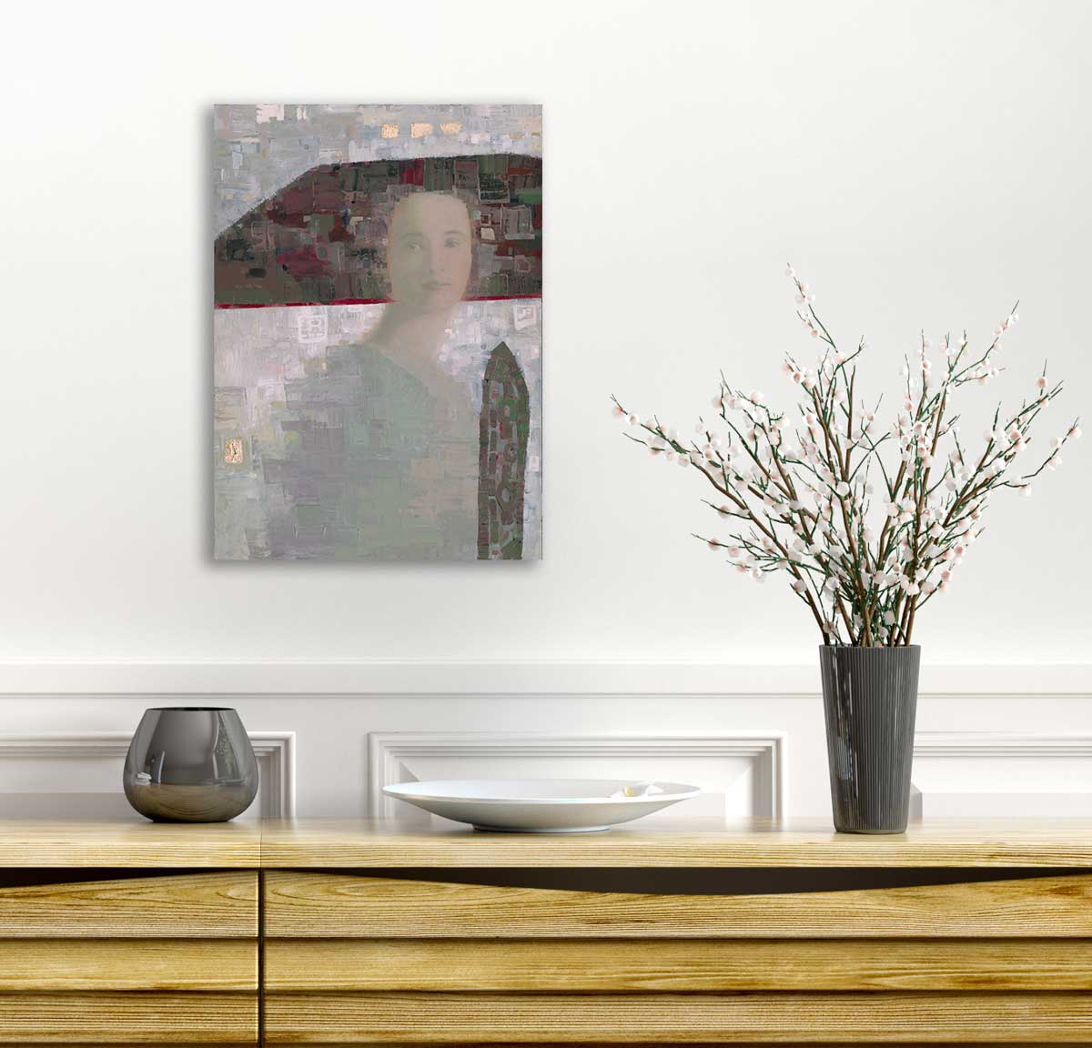 A grey, green and dark red abstracted woman hangs on a white wall above a wooden console table with a grey rounded vase, a white plate and a grey vase with white cherry blossom stems.