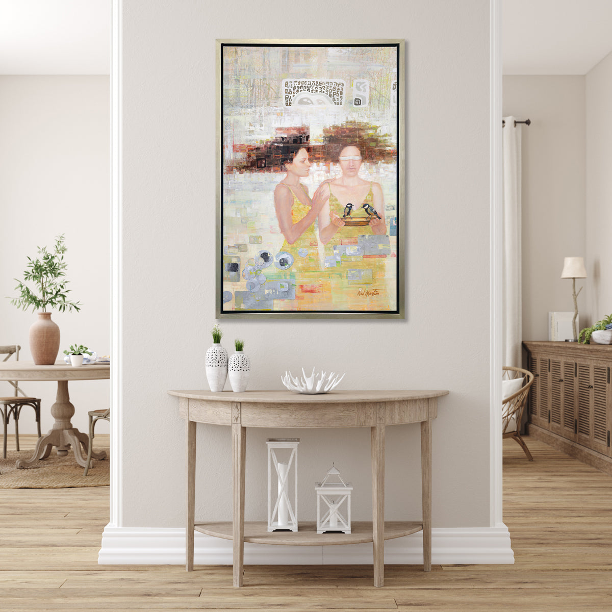 A silver, yellow, and grey abstract figural print in a silver floater frame hangs on a beige wall above a whitewashed half-moon console table with two white vases, a white decorative bowl and two white lanterns.