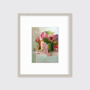 A pink, green and red abstract print in a silver frame with a mat hangs on a white wall.
