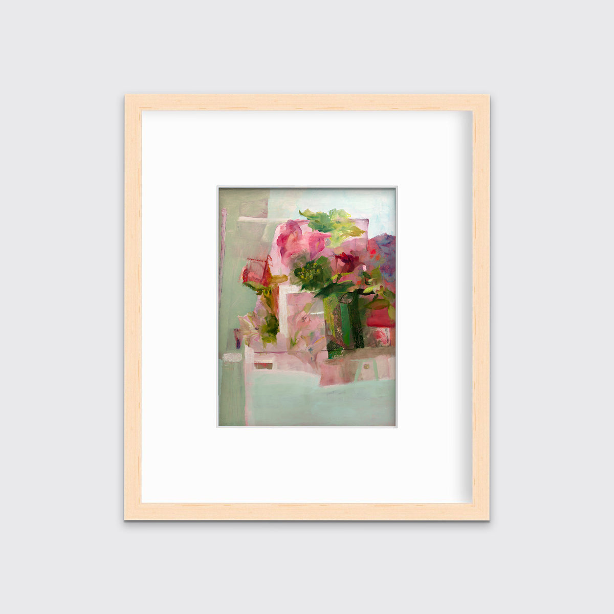 A pink, green and red abstract print in a natural wood frame with a mat hangs on a white wall.