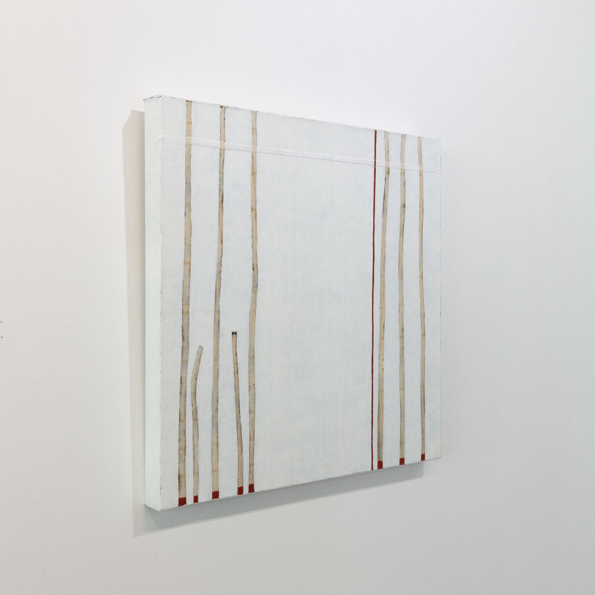 A minimalist painting of beige lines on the right and left of the composition with hints of red on a white background is seen at an angle on a gallery wall.