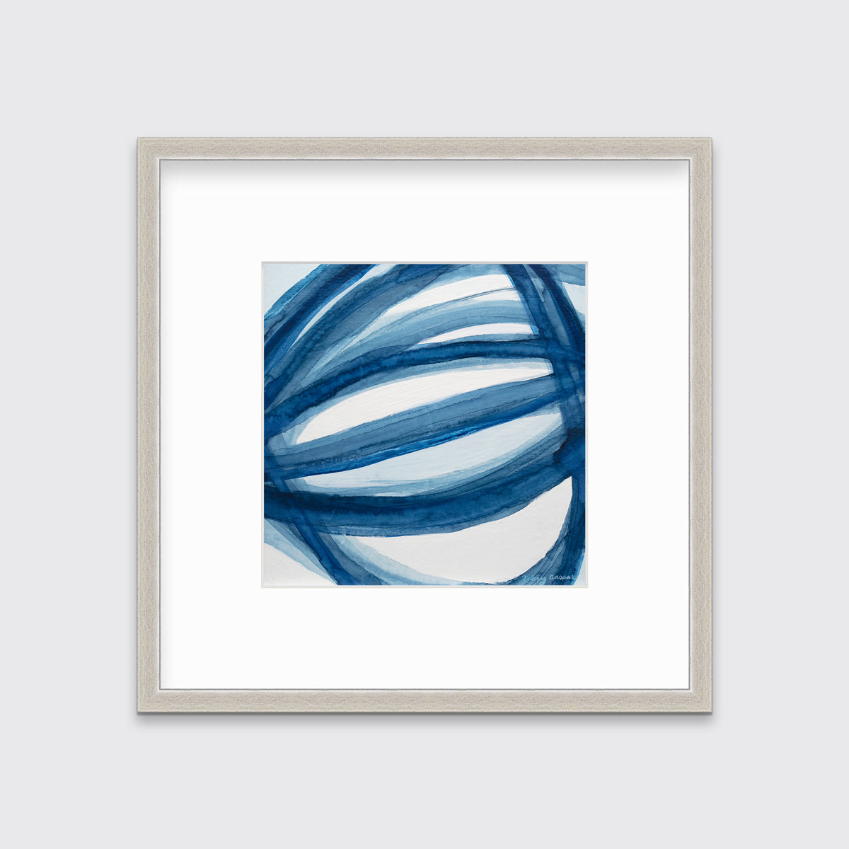 A blue and white abstract print in a silver frame with a mat hangs on a white wall.