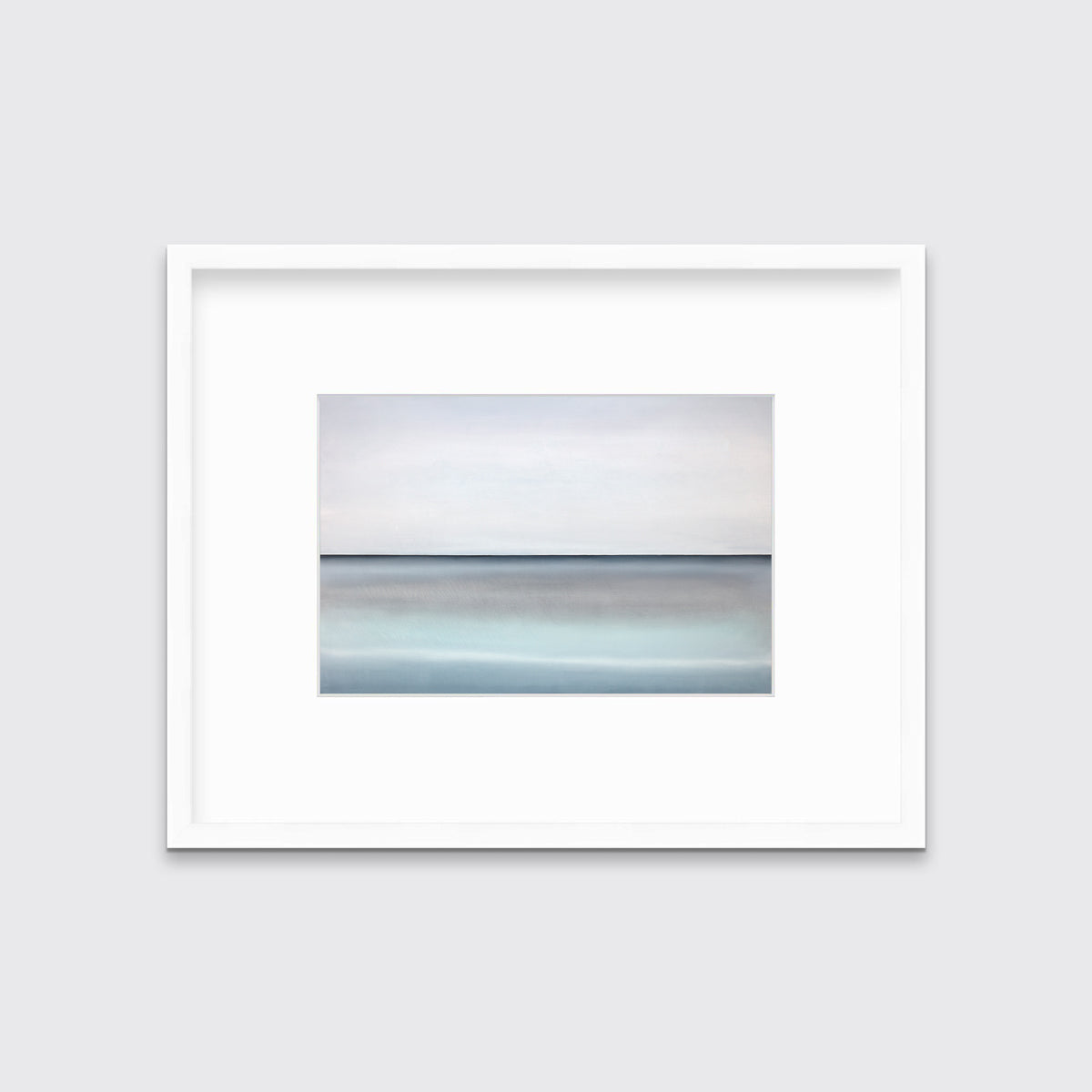 A tonal blue abstract landscape with a defined horizon print in a white frame with a mat hangs on a white wall.