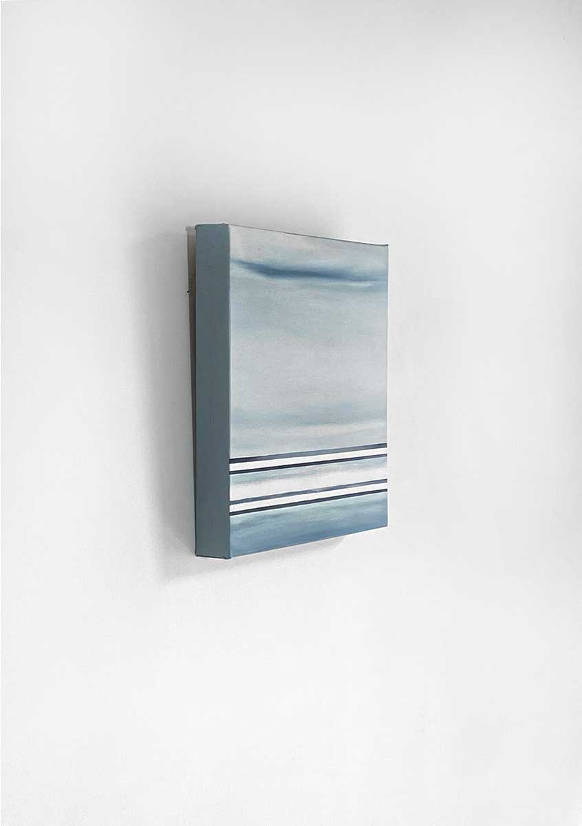 A left side-angle view of a blue and white linear abstract painting hanging on a white wall.