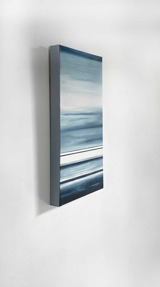 Side angle view of different sized bands of hues of blue and white hanging on a white wall.