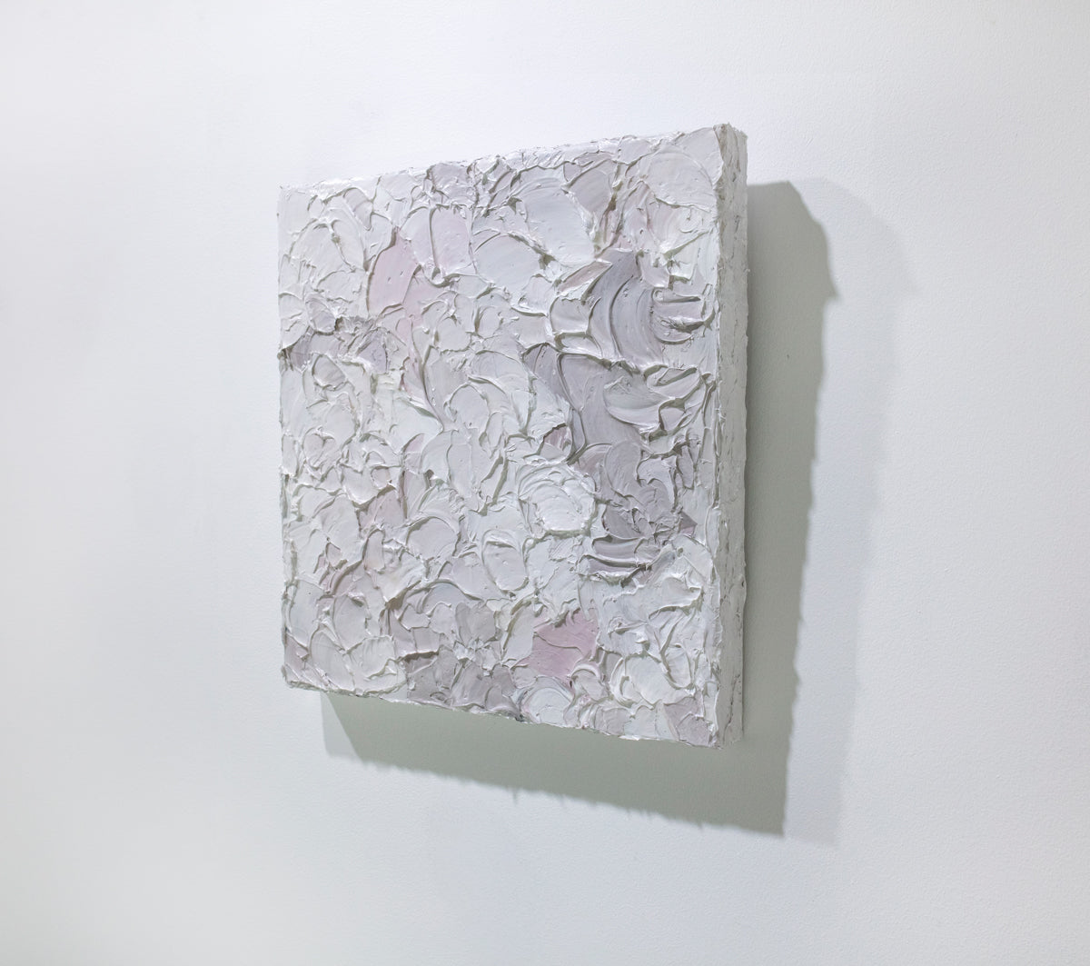 A right angle view of a small abstract painting by Teodora Guererra. It hangs on a white gallery wall.