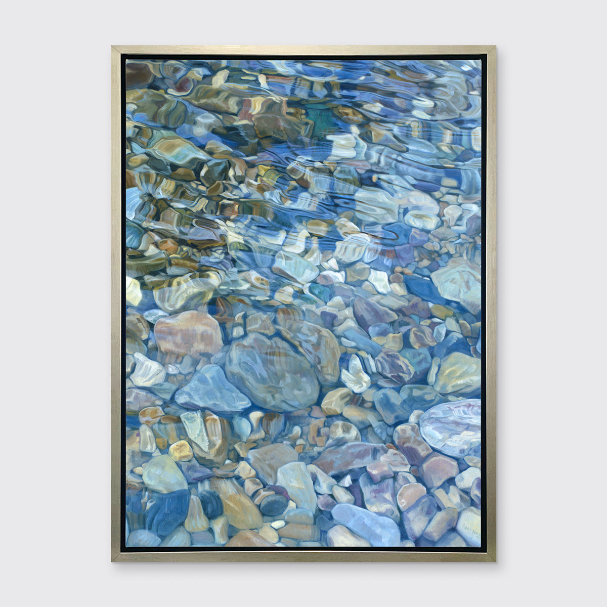 Abstracted river rocks under water hangs in a silver floater frame on a light grey wall.