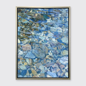 Abstracted river rocks under water hangs in a silver floater frame on a light grey wall.
