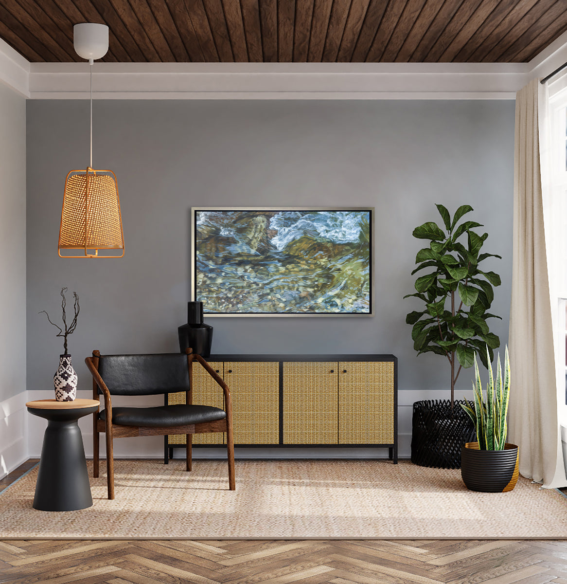 A green, blue, white and tan abstract river rock print in a silver floater frame hangs on a grey wall above a black and tan credenza with a black vase, a black leather and dark wood chair, a black side table and two potted floor plants.