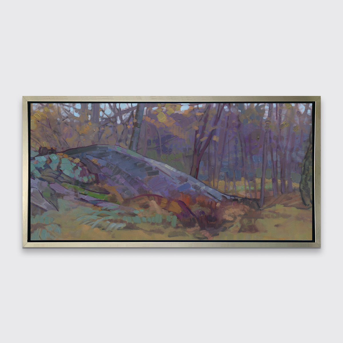A muted multicolored abstract landscape print in a silver floater frame hangs on a white wall.