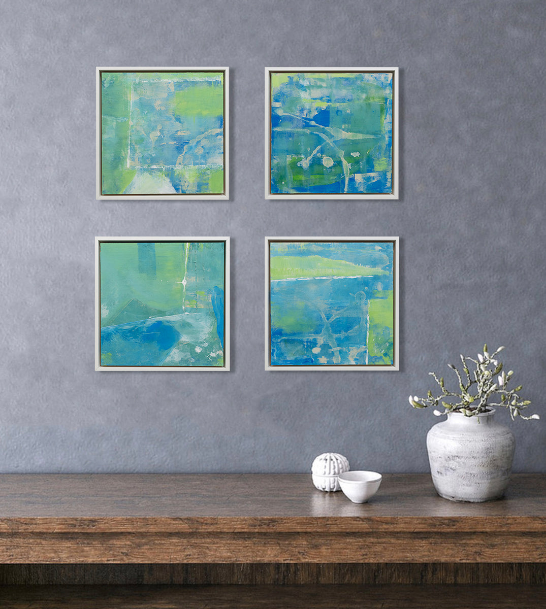 Four abstract paintings with blue and green patches are hung above a console table. Each are wired and ready to hang.