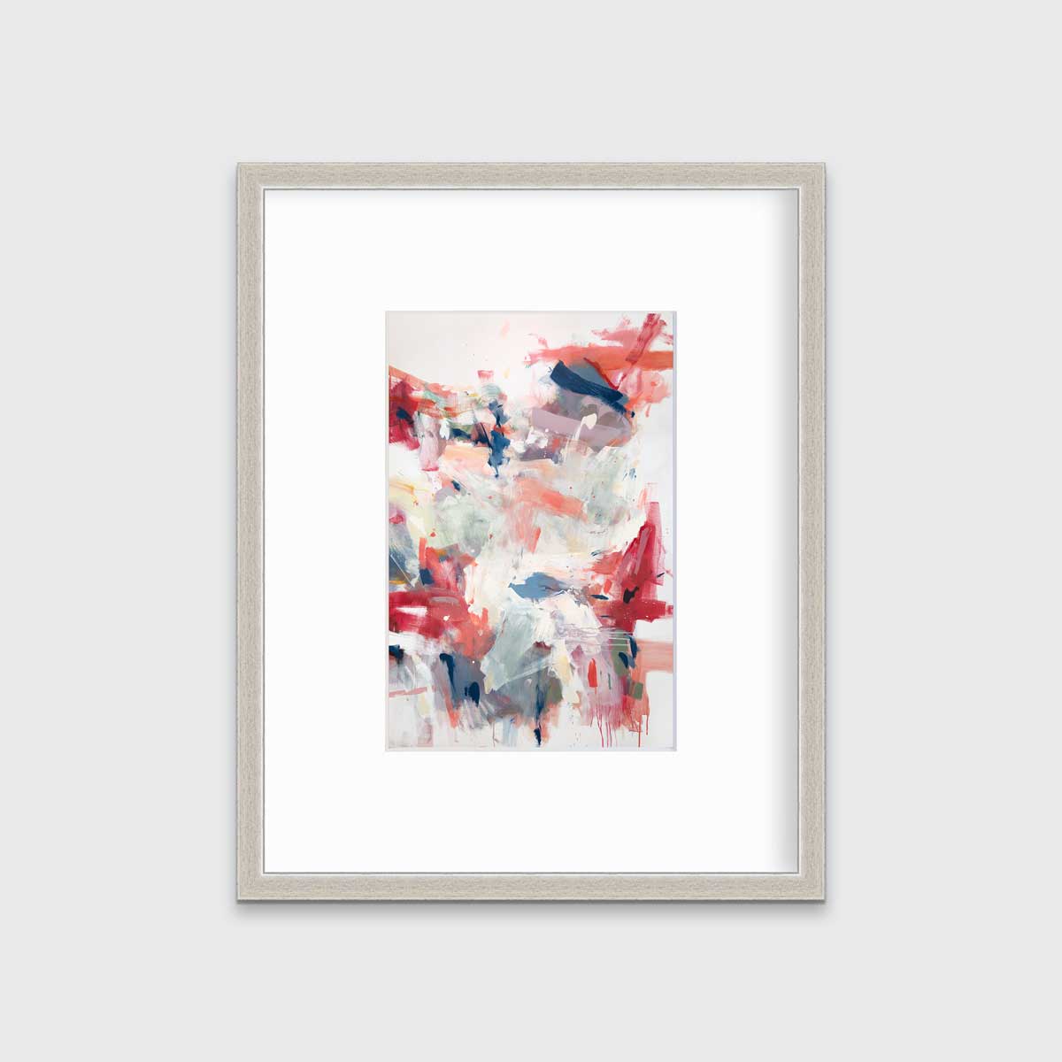A red and white abstract print in a silver frame with a mat hangs on a white wall.
