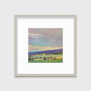 A blue, green and purple abstract landscape print in a silver frame with a mat hangs on a white wall.