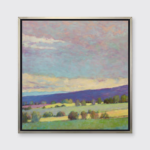 A blue, green and purple abstract landscape print in a silver floater frame hangs on a white wall.