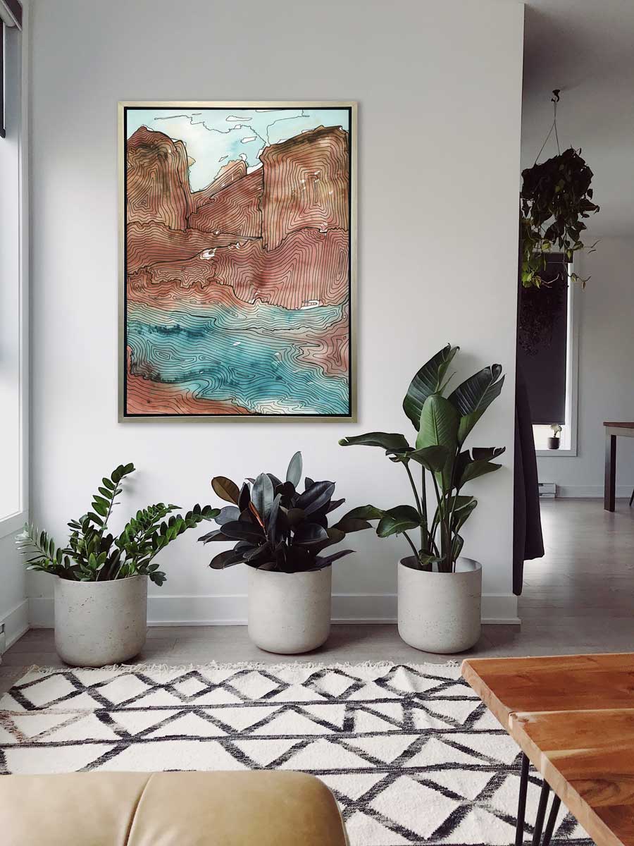 A teal, brown and black abstract landscape print in a silver floater frame hangs on a white wall above three various size potted plants.