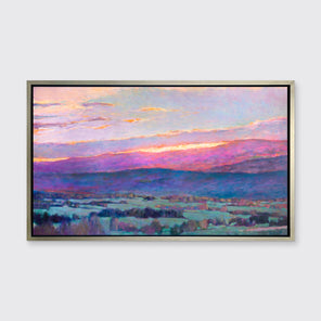 A pink, blue and green abstract landscape print in a silver floater frame hangs on a white wall.