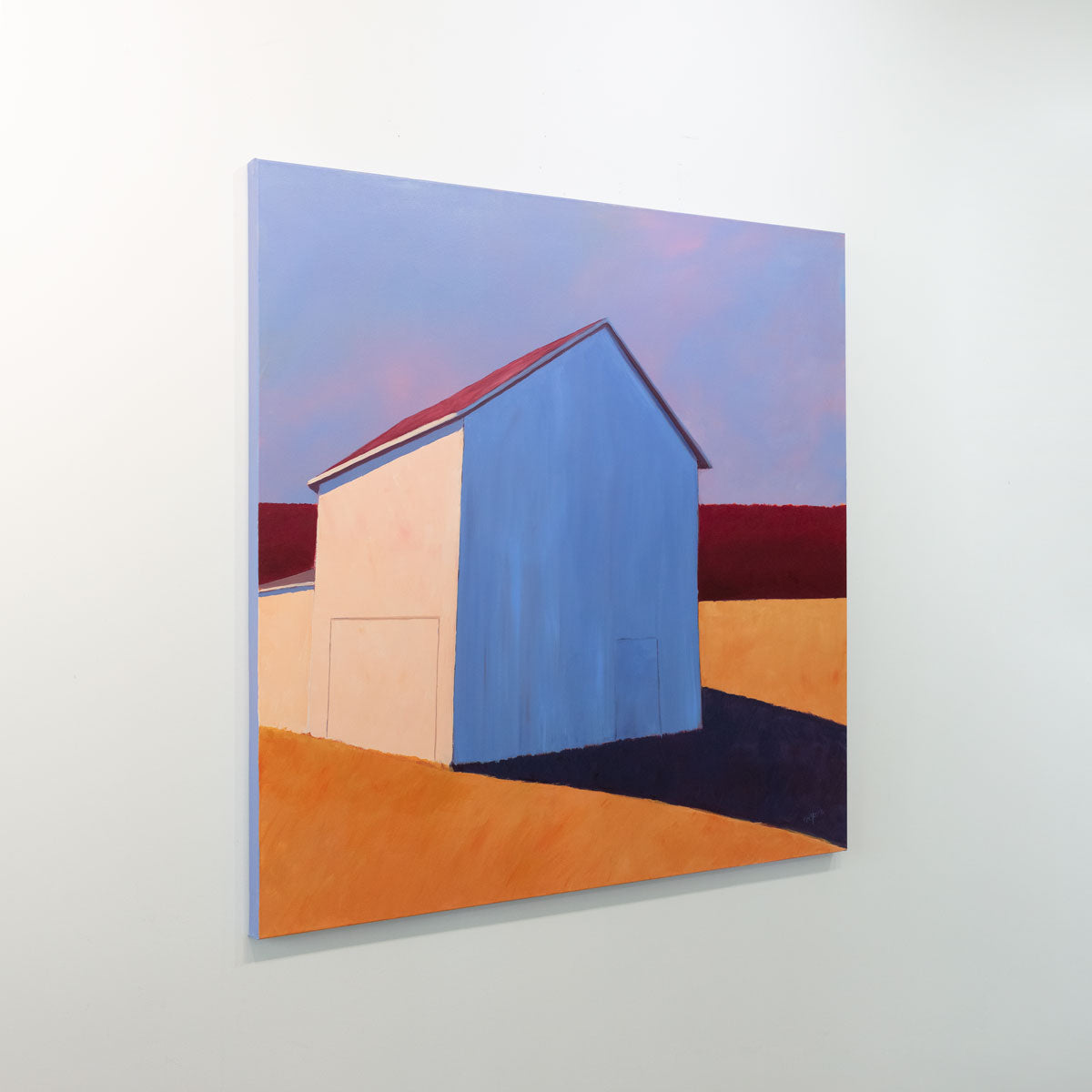 A painting of a white barn casting a long shadow is seen at an angle on a gallery wall.