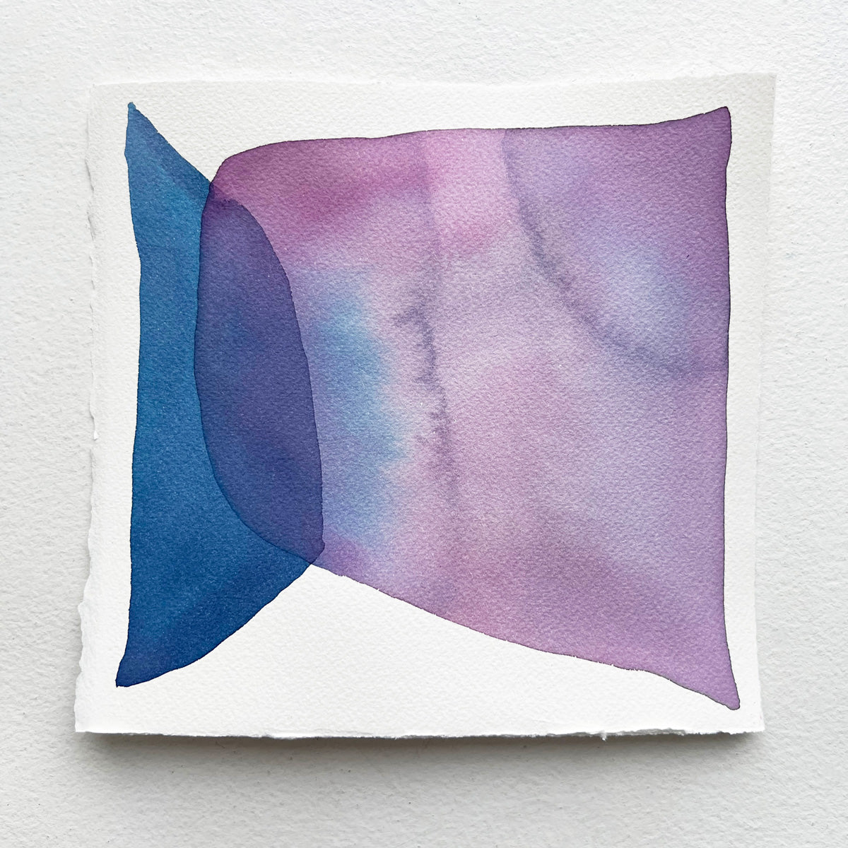 A blue and violet abstract watercolor painting on paper rests on a white surface. 