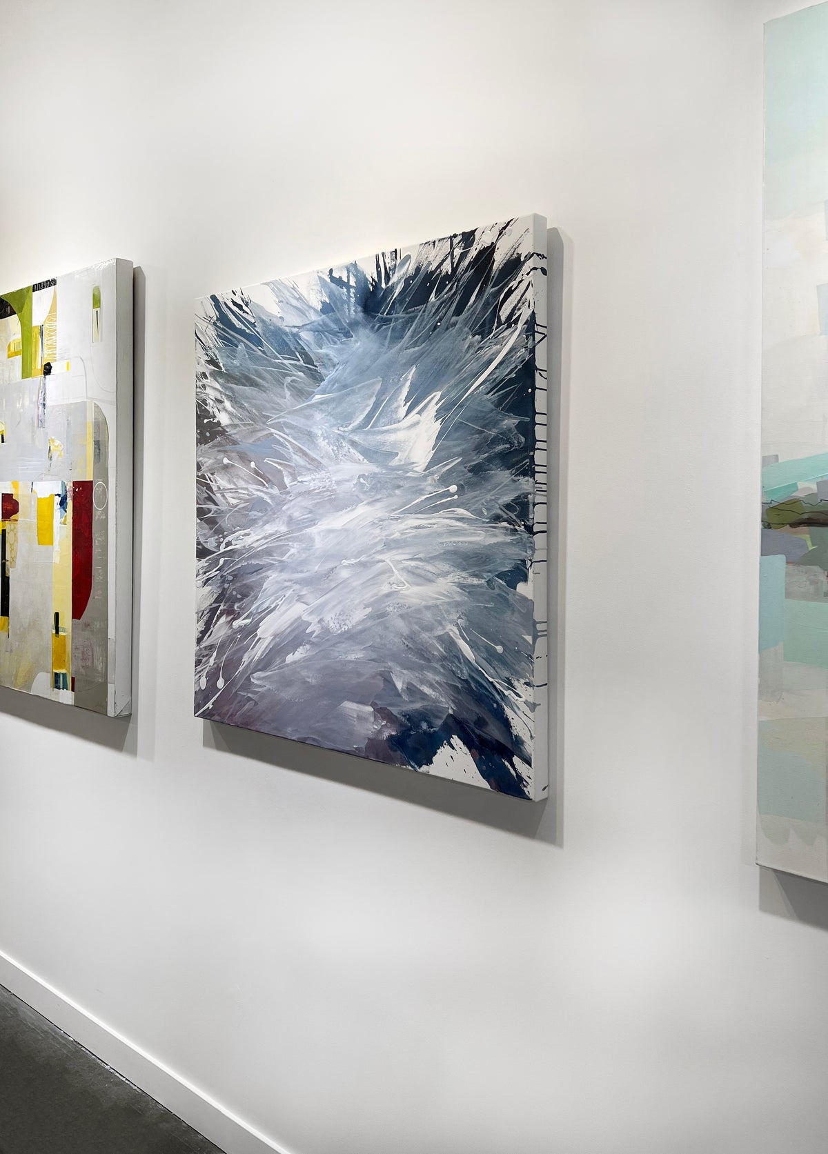 A white, blue, and lavender abstract painting by Teodora Guererra hangs on a white wall, viewed from the right. 