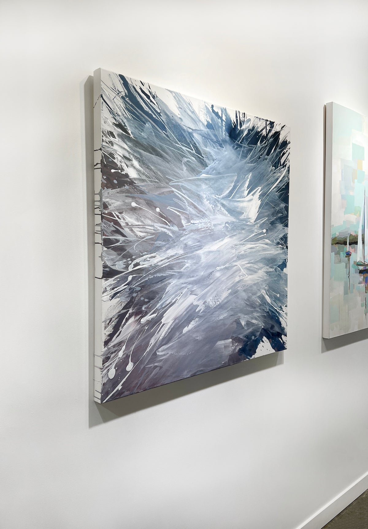 A white, blue, and lavender abstract painting by Teodora Guererra hangs on a white wall, viewed from the left. 