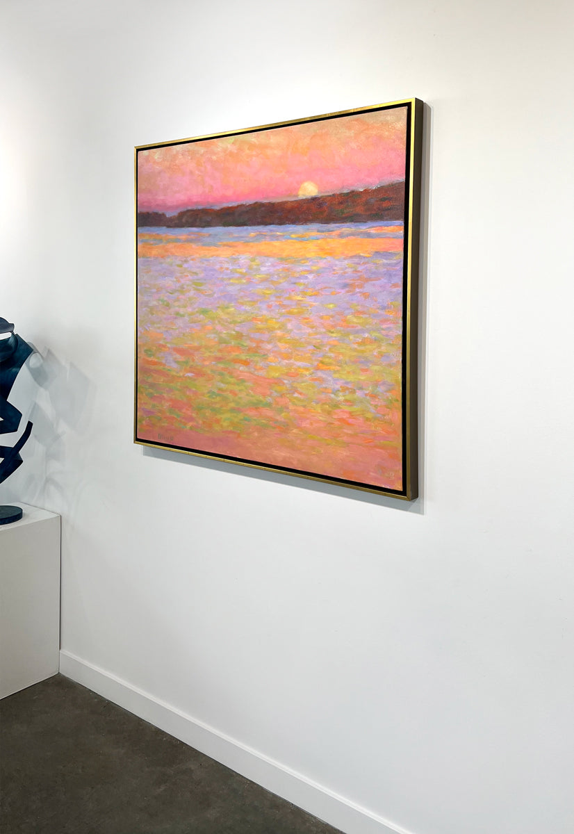 Framed painting of a sunset over water with a colorful sky hanging on a white wall side view.