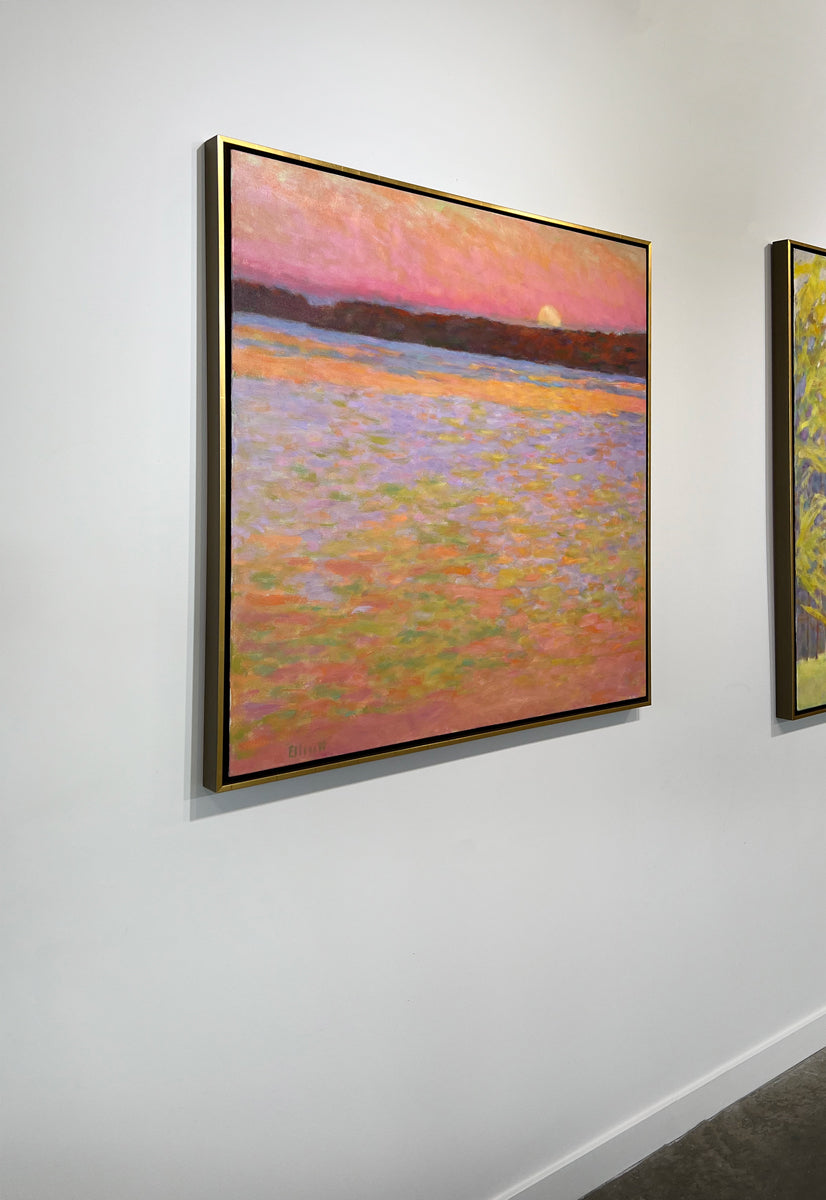 Framed painting of a sunset over water with a colorful sky hanging - side view on a white wall.