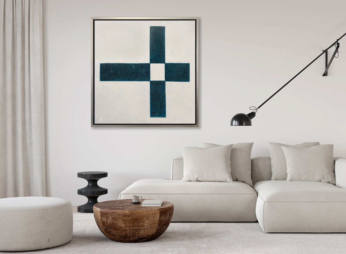 A beige and teal abstract geometric print in a silver floater frame hangs on a white wall above a white sectional sofa with pillows, a rounded wood coffee table, a black wall mounted movable light and a white ottoman.