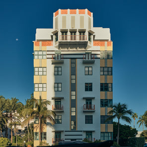An art deco building in Miami Beach, Florida at sunset with a blue sky, palm trees, and the moon to the left. 
