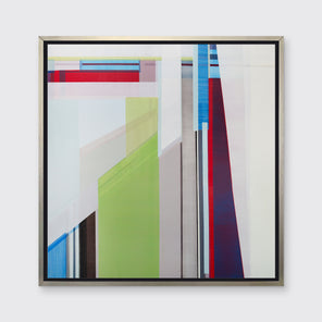 A green, blue, red, and grey geometric print in a silver floater frame hangs on a white wall.