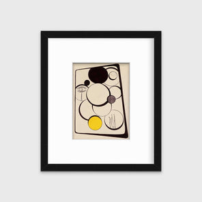 An abstract, geometric print with smaller images within the larger geometric shapes in a black frame with a mat hangs on a white wall.