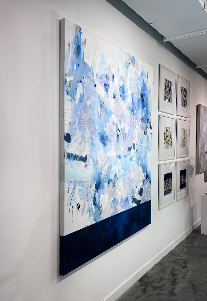 A blue, white, and purple abstract painting by Kelly Rossetti hangs vertically on a white wall in the gallery, viewed from the left. 