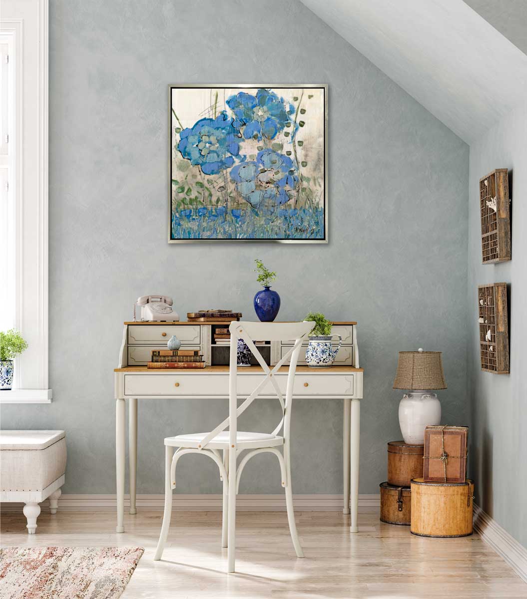 A blue and beige floral print in a silver floater frame hangs on a grey wall above a two-tiered desk with a white rotary phone, some blue vases with greenery and a white chair.