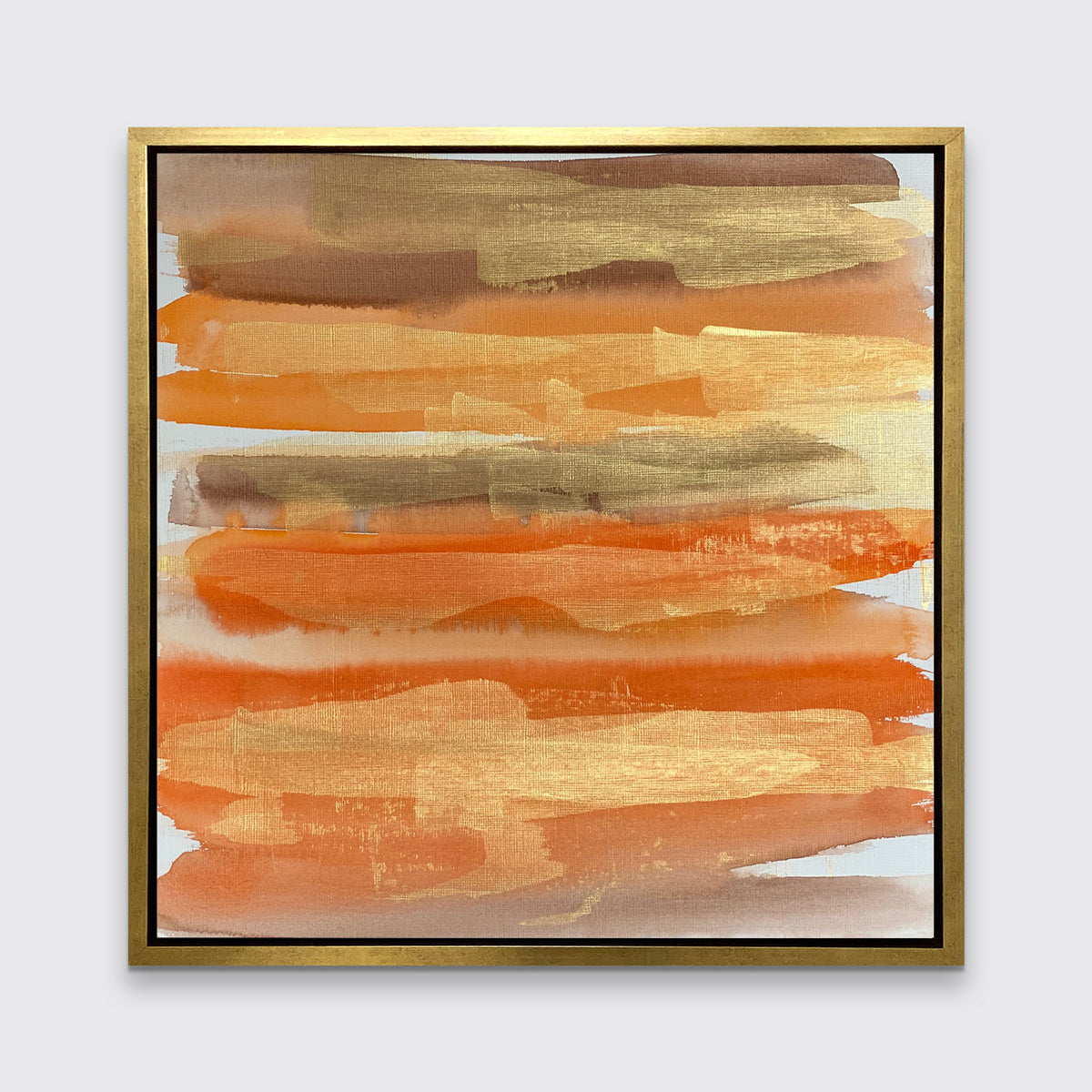 A gold, orange and light brown abstract print in a gold floater frame hangs on a white wall.
