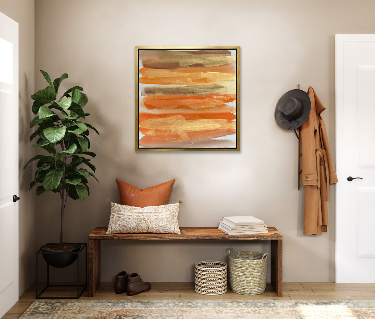 A gold, orange and light brown abstract print in a gold floater frame hangs on a white wall above a live edge bench with pillows and a stack of books, a potted floor plant and two woven baskets.