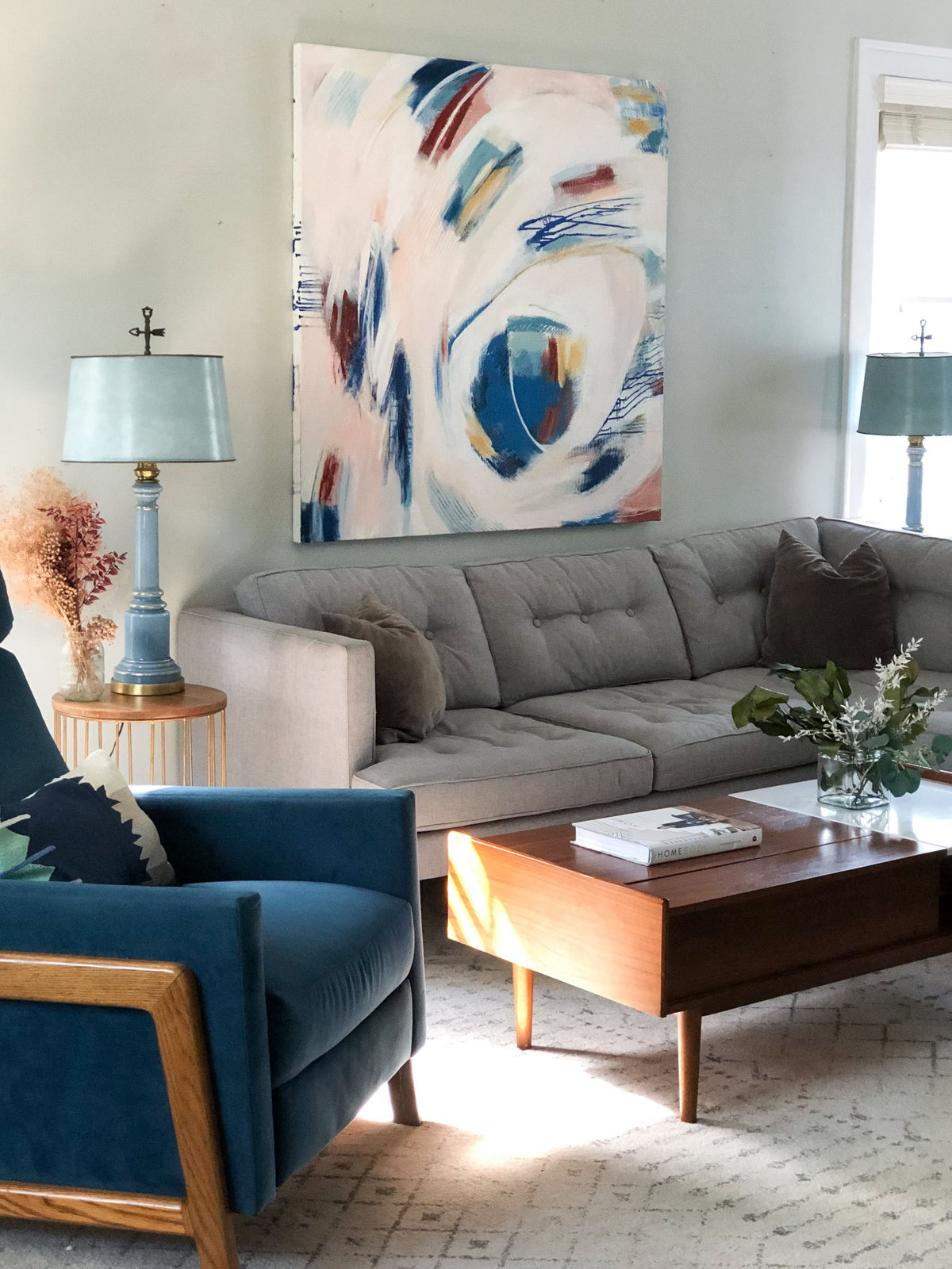 Mary Gaspar's painting, Touch, hanging on a light grey wall above a grey sectional and dark blue accent chair.