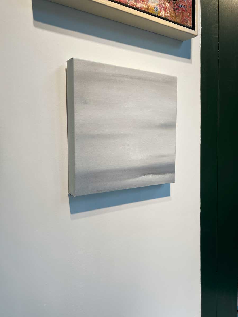 A left side-angle view of a tonal grey abstract painting by Tony Iadicicco hangs on a white wall.