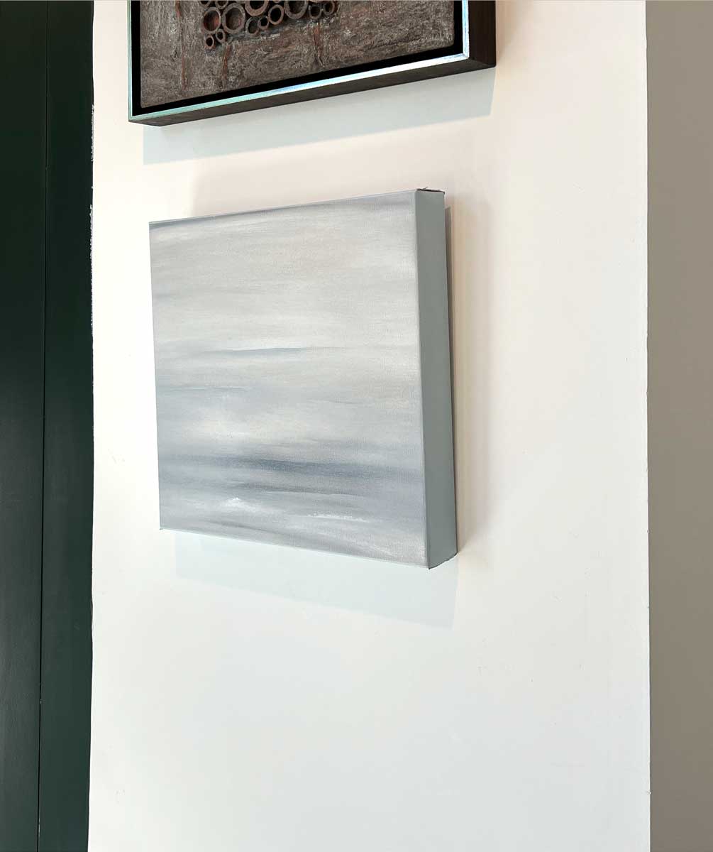 A right side-angle view of a tonal grey abstract painting by Tony Iadicicco hangs on a white wall.