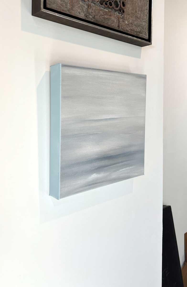 A left side-angle view of a tonal grey abstract painting by Tony Iadicicco hangs on a white wall.
