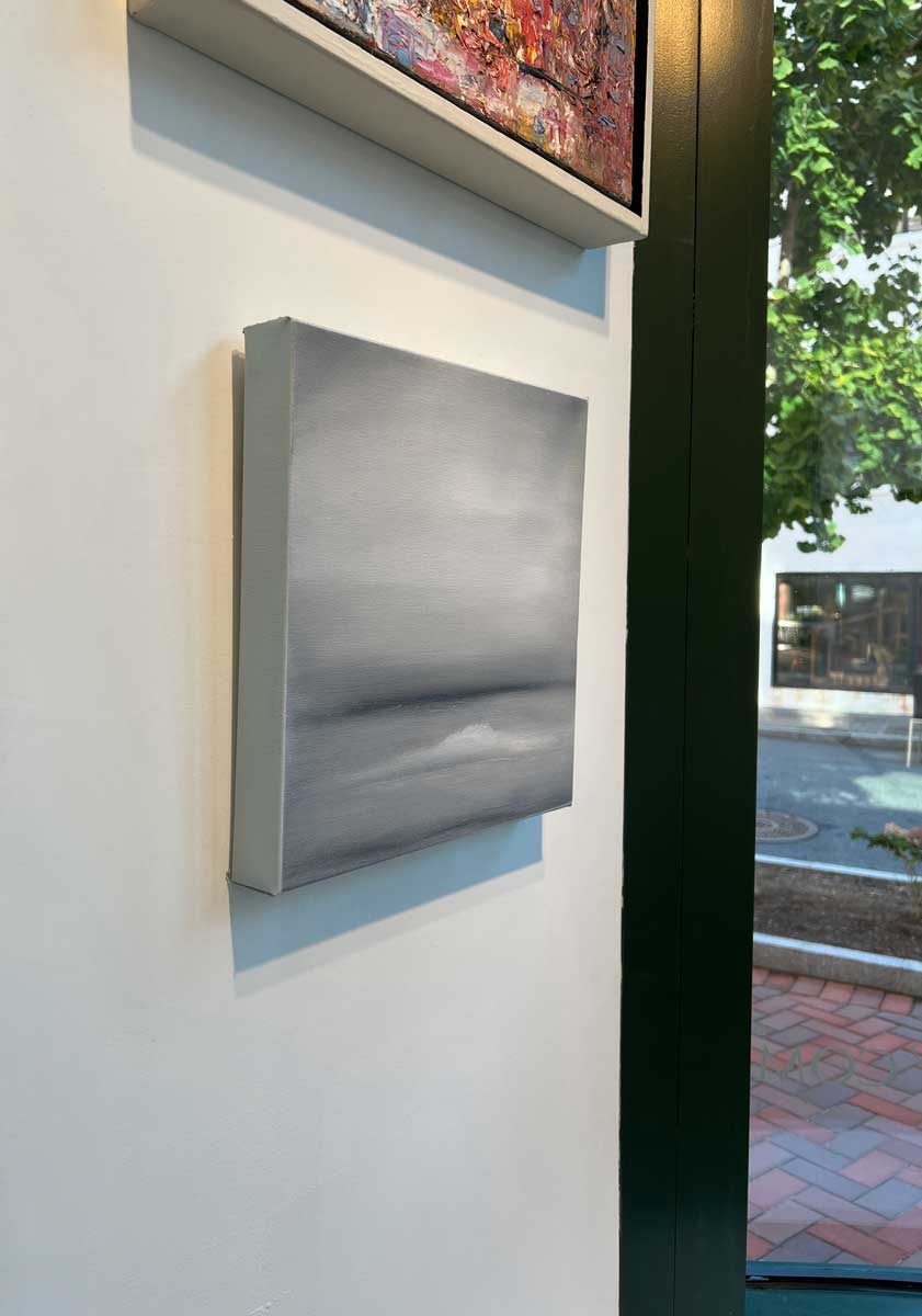 A left side-angle view of a tonal grey abstract painting by Tony Iadicicco hangs on a white wall.