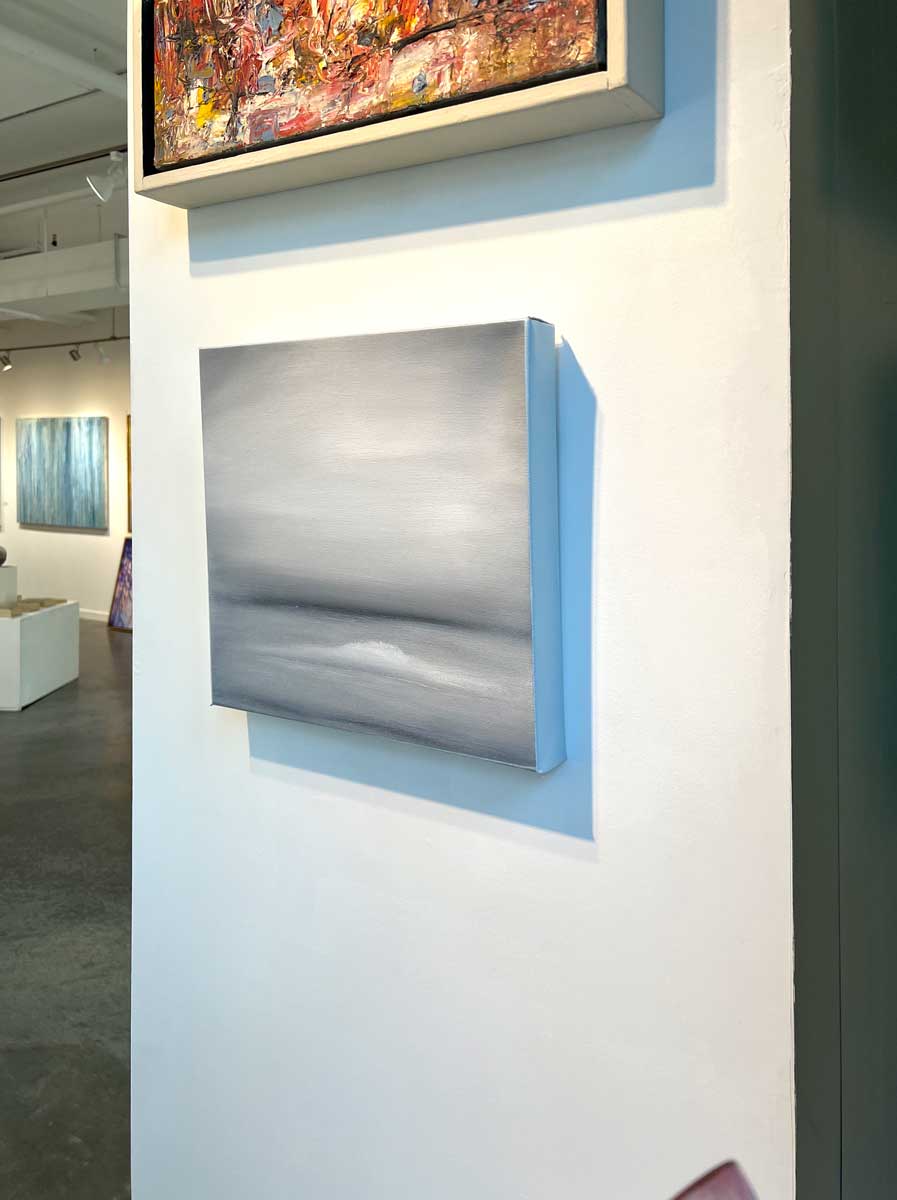 A right side-angle view of a tonal grey abstract painting by Tony Iadicicco hangs on a white wall.